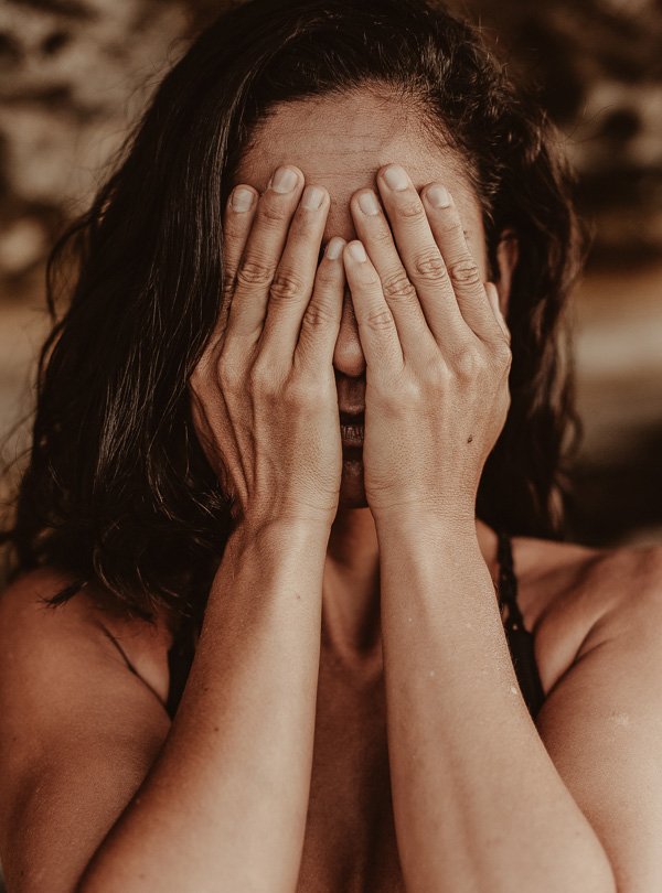Frau mit Händen vor dem Gesicht, symbolisiert Stress und Hautprobleme, in Zusammenhang mit den Auswirkungen von Stress auf die Hautgesundheit.