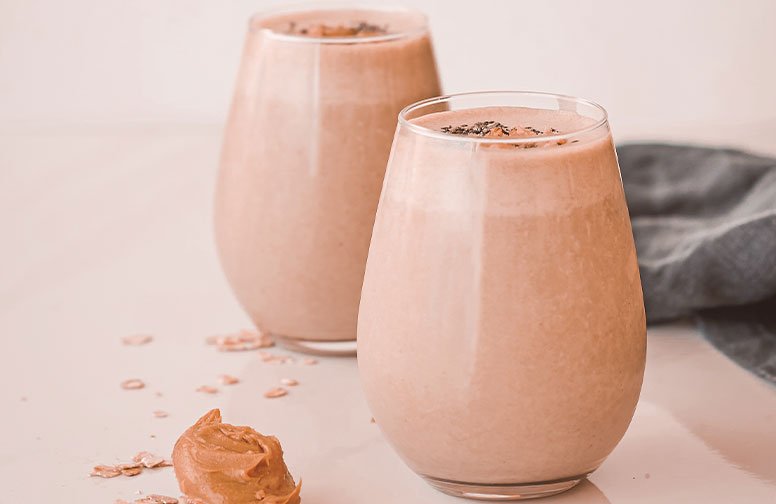 Zwei Gläser cremiger Smoothies mit Haferflocken und Erdnussbutter, dekoriert mit Samen, auf einem hellen Tisch, passend zu winterlichen Vitaminrezepten für ein starkes Immunsystem.