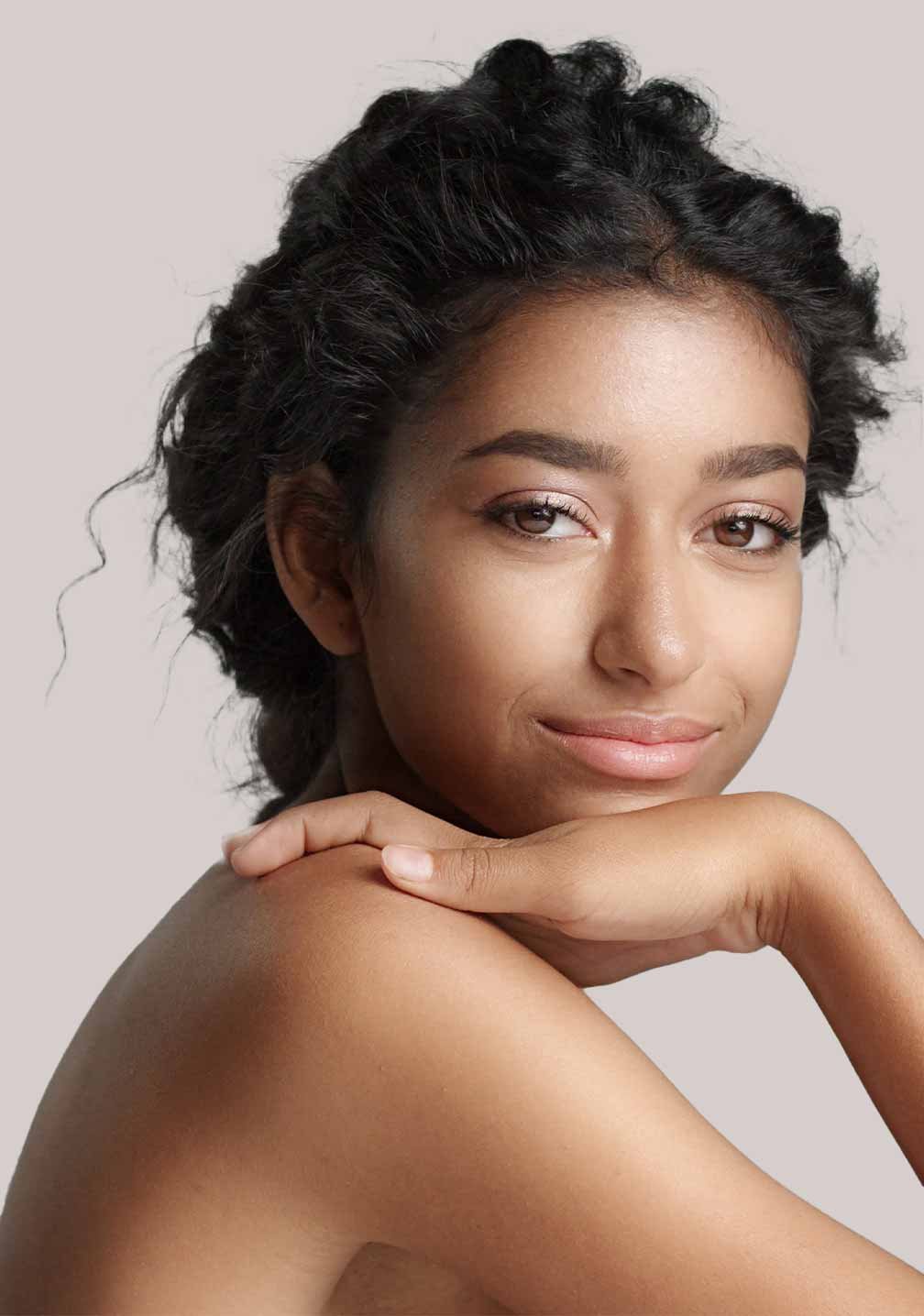 Frau mit dunkler Haut und lockigem Haar, lächelnd, zeigt strahlenden Teint, repräsentiert BB Cream Perfect Care Bronze von RAU Cosmetics.