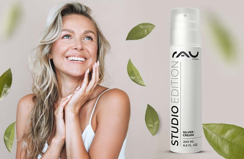 Frau mit blonden Wellenhaaren zeigt RAU Silvercream 200 ML, umgeben von grünen Blättern für schöne Haut.