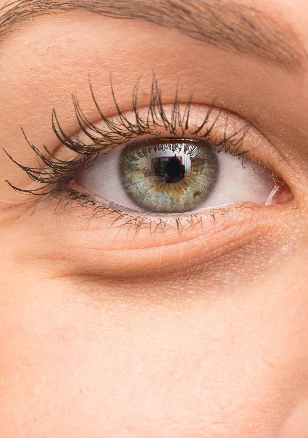 Nahaufnahme eines menschlichen Auges mit einem detaillierten, grünen und braunen Iris, umgeben von langen Wimpern.